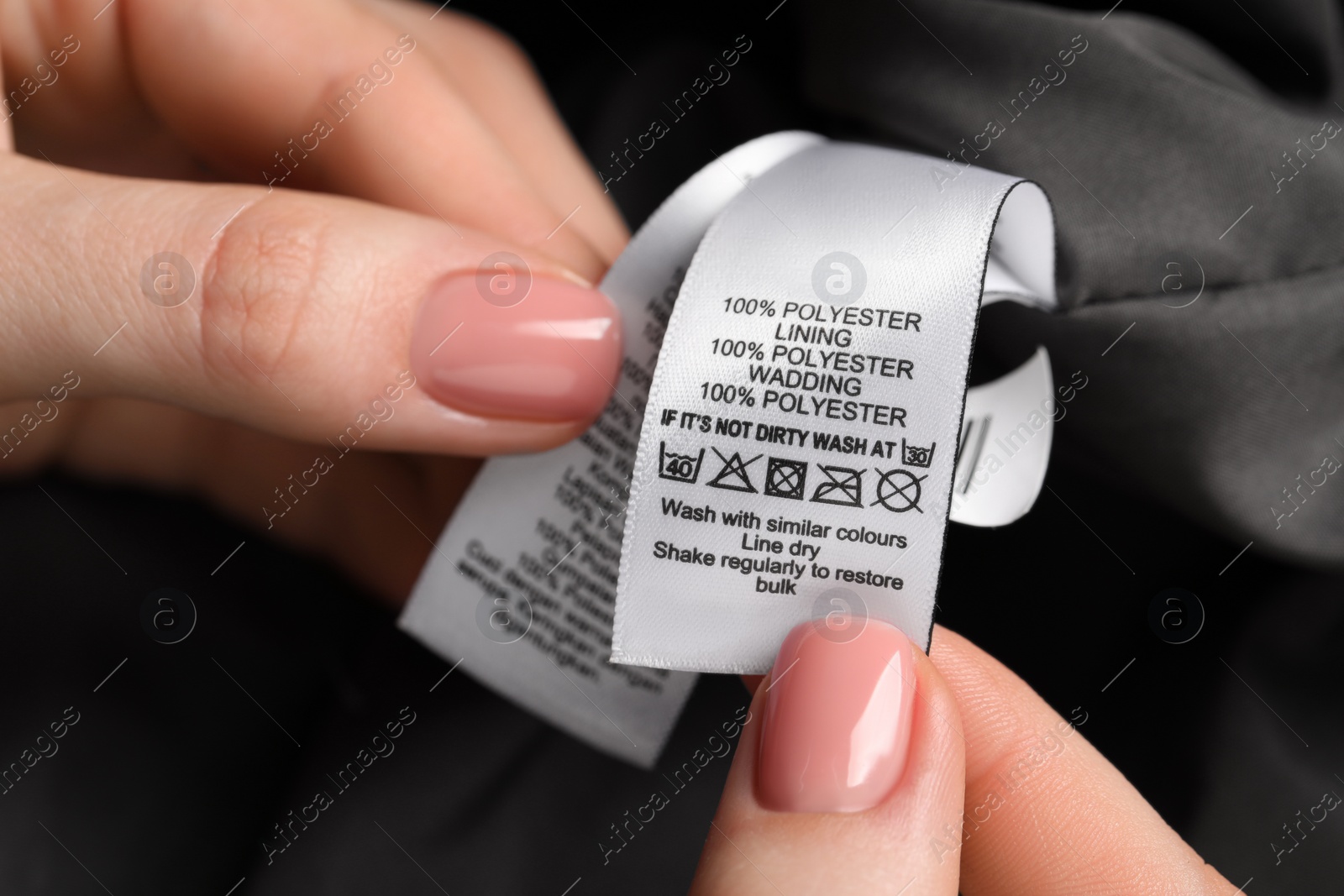 Photo of Woman holding clothing labels on black garment, closeup