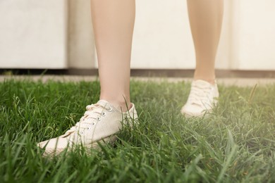 Photo of Woman in stylish sneakers walking on green grass outdoors, closeup