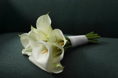 Photo of Beautiful calla lily flowers tied with ribbon on sofa