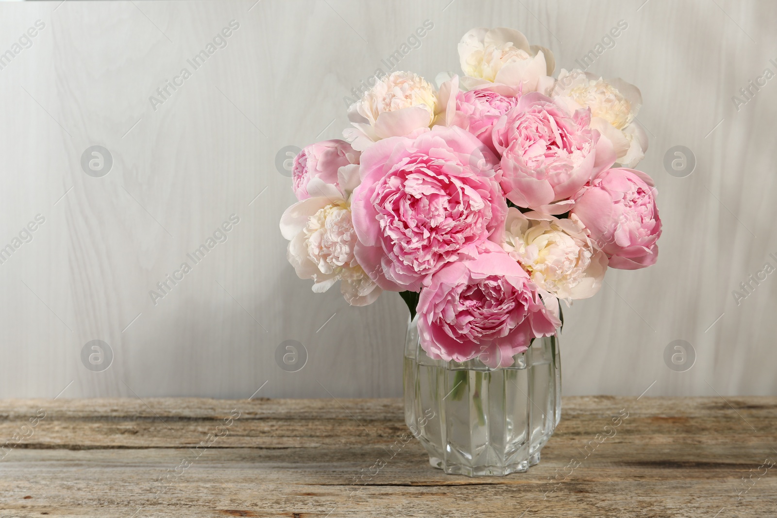 Photo of Beautiful peonies in vase on wooden table, space for text