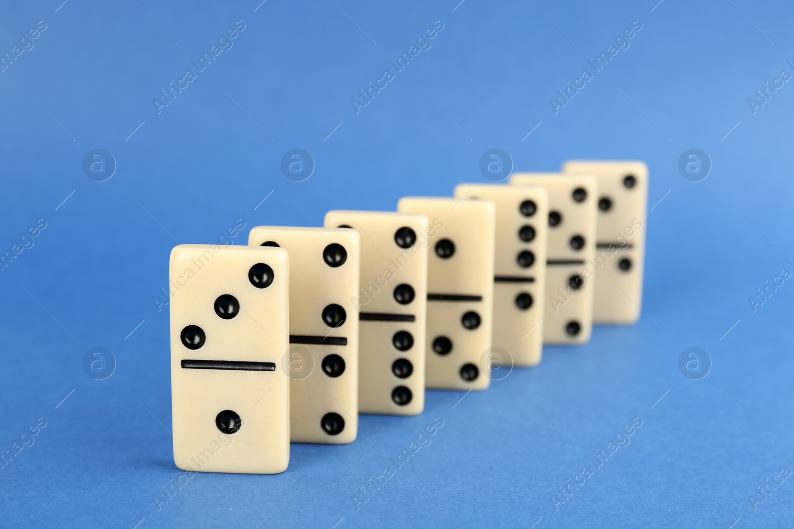 Photo of Row of white domino tiles on blue background