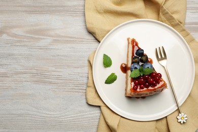 Photo of Slice of delicious cheesecake served with berries and caramel sauce on white wooden table, flat lay. Space for text