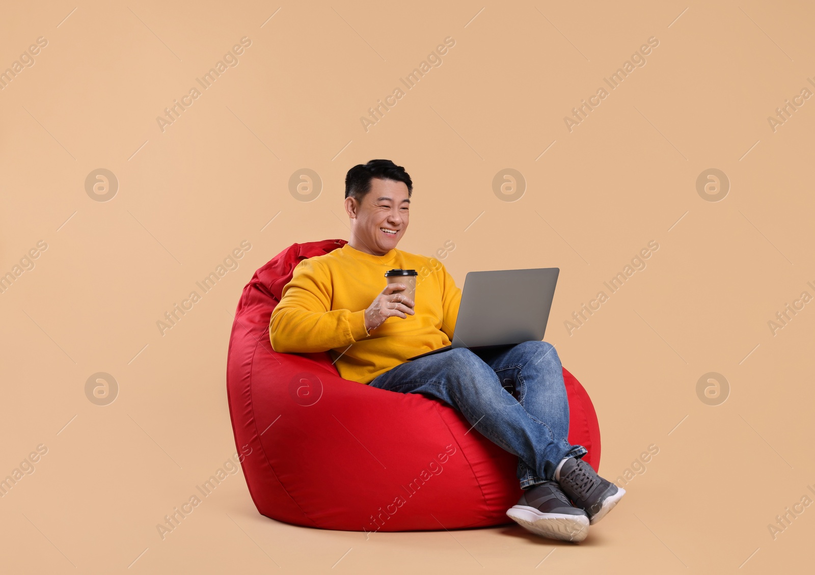 Photo of Happy man with laptop and coffee on beige background