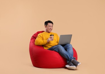 Happy man with laptop and coffee on beige background