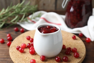 Photo of Cranberry sauce in pitcher and fresh berries on wooden table