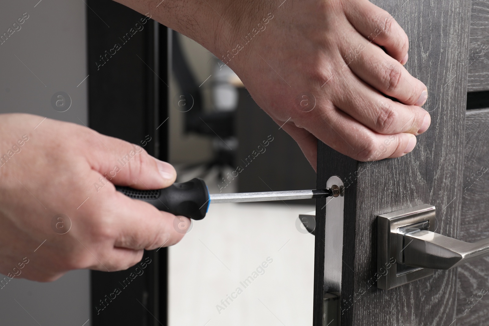 Photo of Handyman with screwdriver repairing door handle indoors, closeup