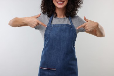 Photo of Woman pointing at kitchen apron on light grey background, closeup. Mockup for design