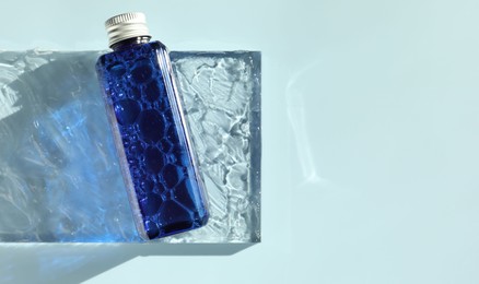 Bottle of cosmetic product on light blue background, top view. Space for text