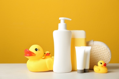 Photo of Baby cosmetic products, toys and accessories on white table against yellow background