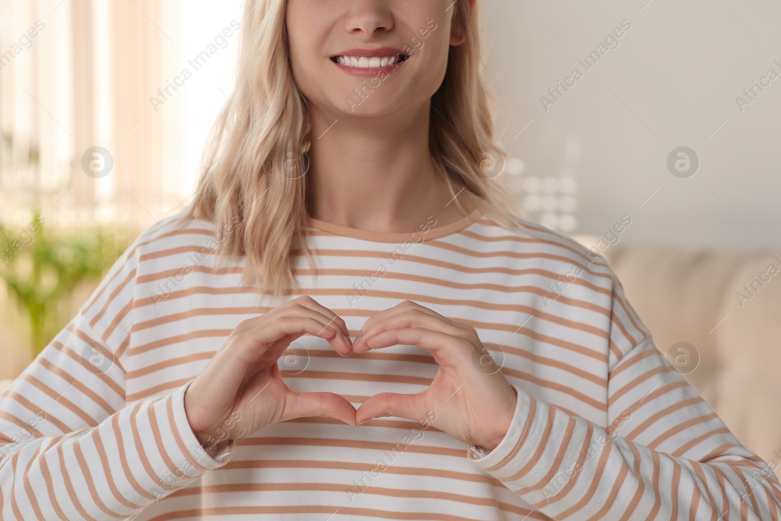 Photo of Happy volunteer making heart with her hands in room, closeup