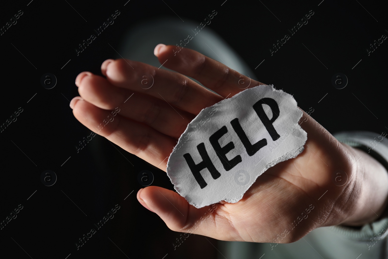 Photo of Woman holding piece of paper with word Help on black background, closeup. Domestic violence concept