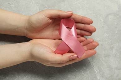 Photo of Woman with pink ribbon at grey marble table, closeup. Breast cancer awareness