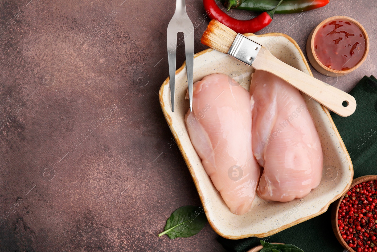 Photo of Marinade, basting brush, raw chicken fillets and spices on brown table, flat lay. Space for text