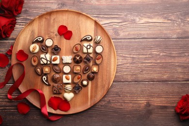 Heart made with delicious chocolate candies and rose petals on wooden table, top view. Space for text