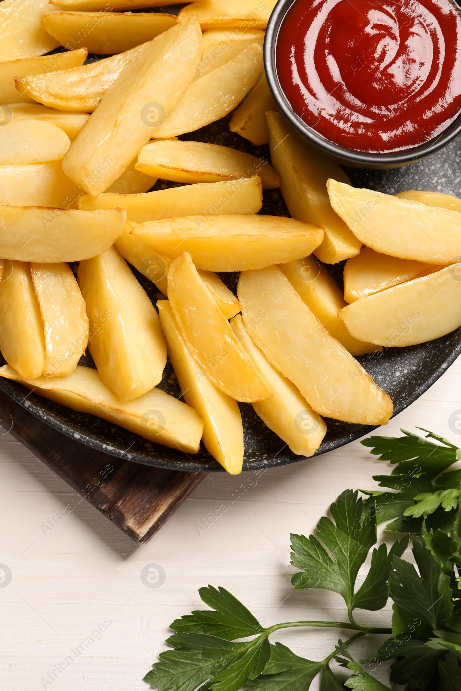 Photo of Pan with tasty baked potato wedges and sauce on white wooden table, flat lay