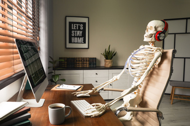 Human skeleton with headphones using computer at workplace