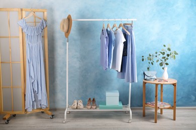 Rack with stylish clothes near light blue wall indoors