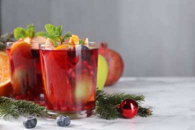 Photo of Aromatic Sangria drink in glasses, ingredients and Christmas decor on white marble table, space for text