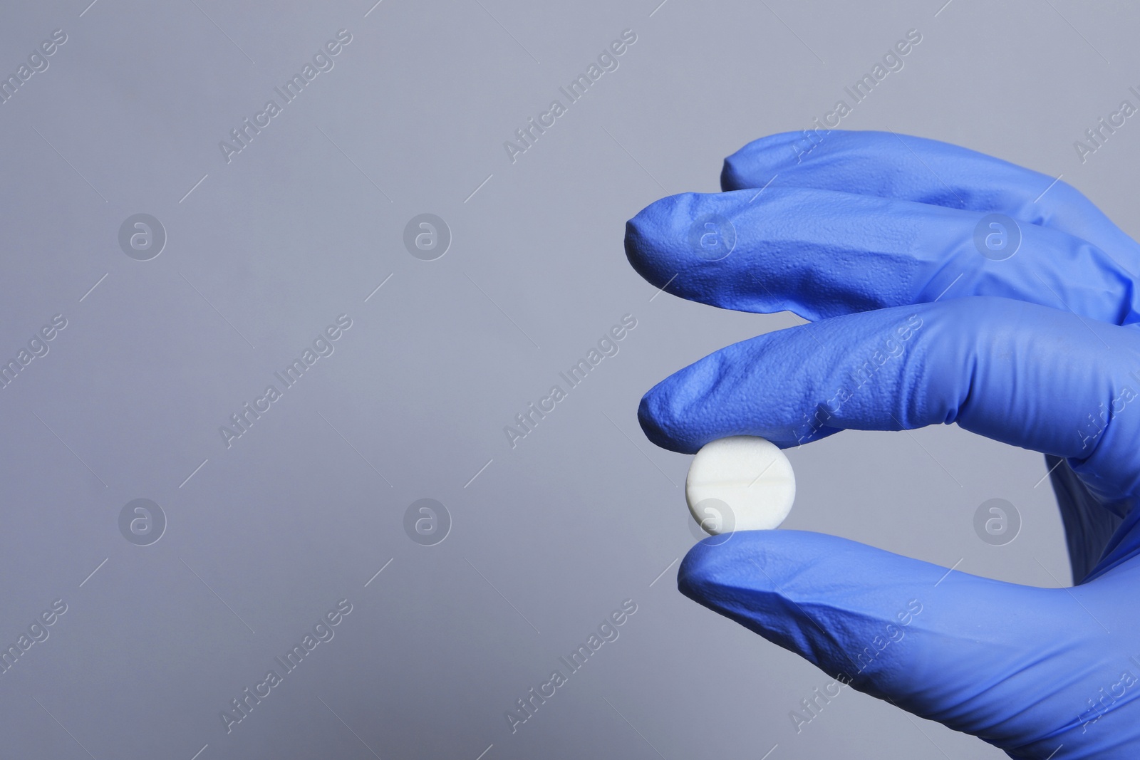 Photo of Doctor holding pill on grey background, closeup. Space for text