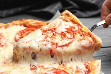 Woman taking slice of hot cheese pizza Margherita on table, closeup