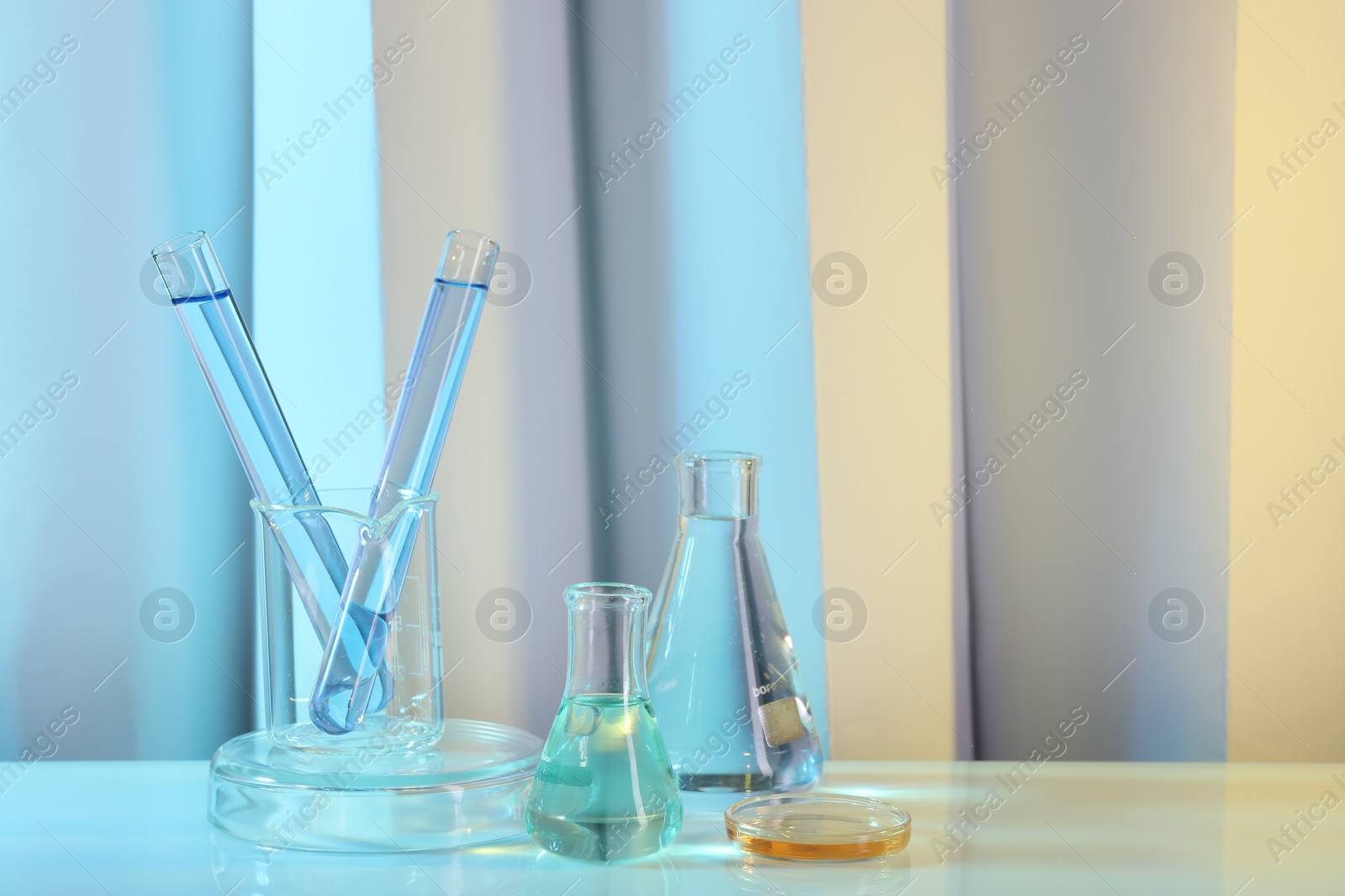 Photo of Laboratory analysis. Different glassware on table against color background, space for text