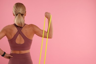 Photo of Woman exercising with elastic resistance band on pink background, back view. Space for text