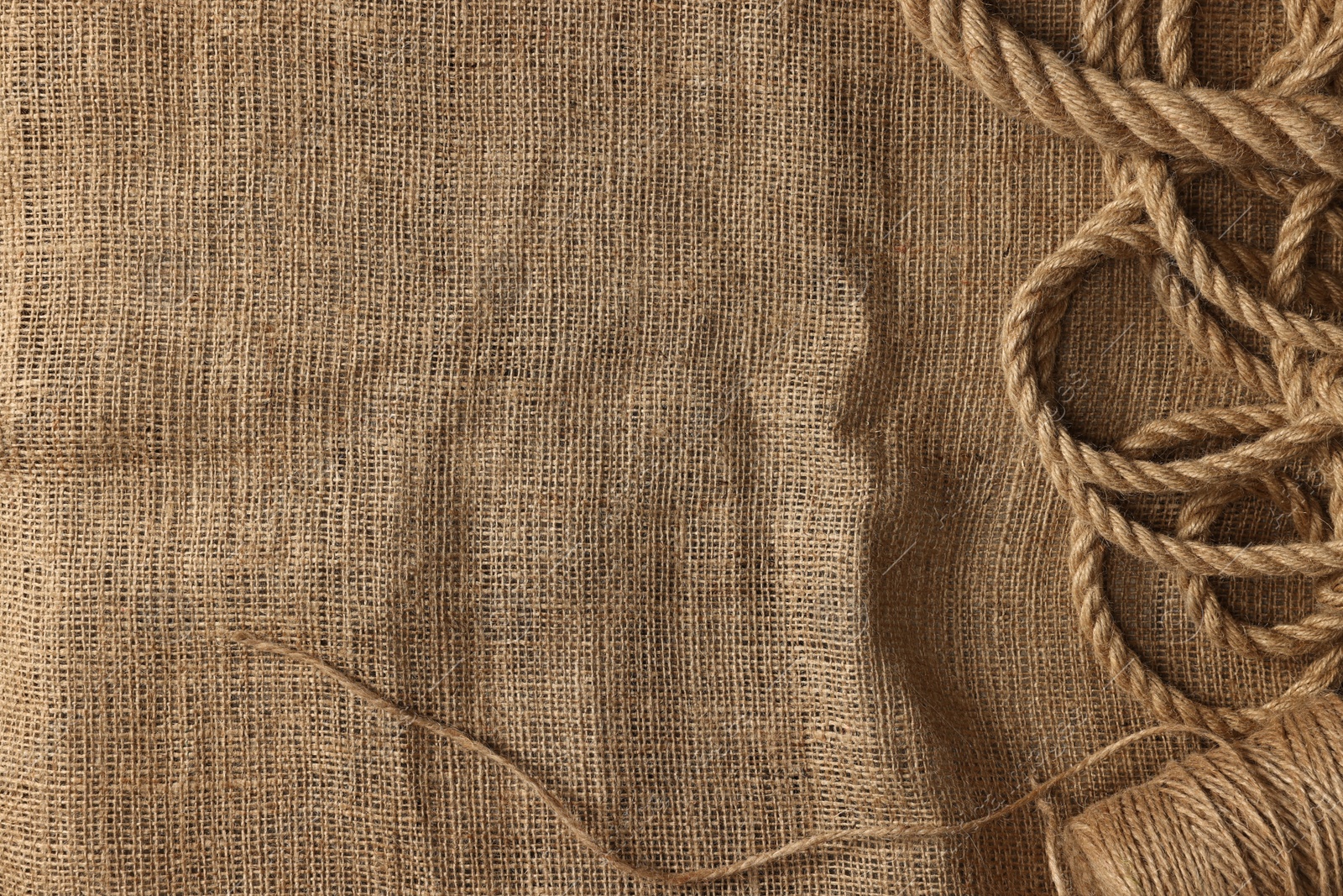 Photo of Spool of thread and jute on burlap fabric, top view