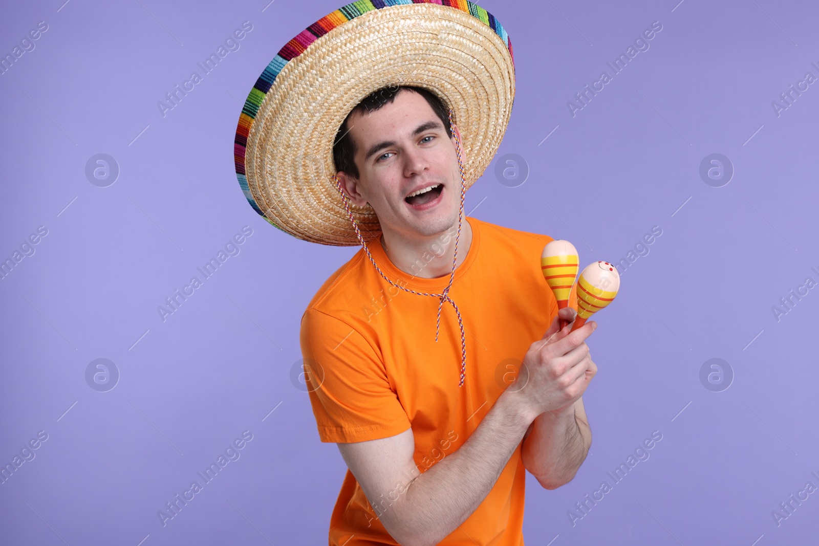 Photo of Young man in Mexican sombrero hat with maracas on violet background