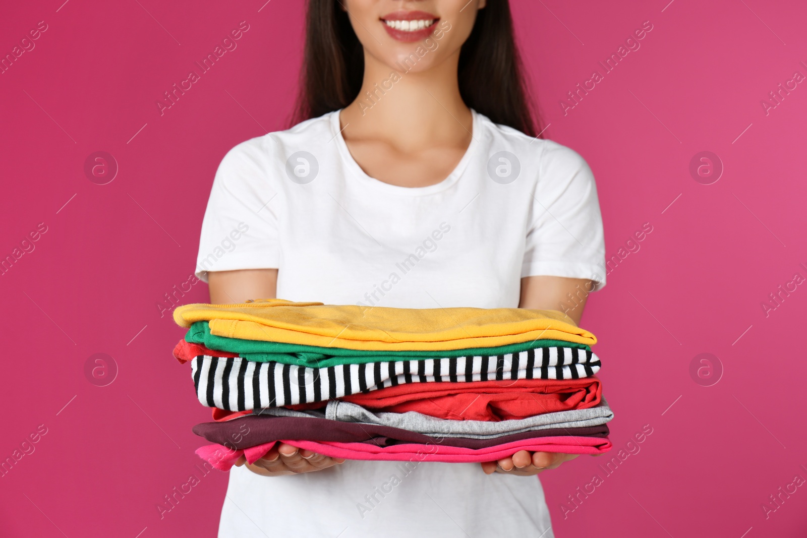 Photo of Young woman holding clean laundry on color background, closeup