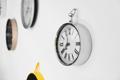 Photo of Stylish clock with Roman numerals on white wall. Time of day