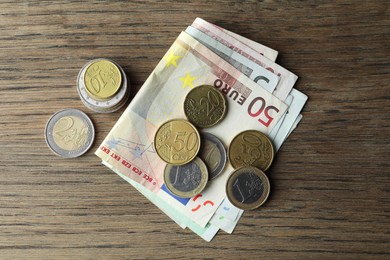 Photo of Euro banknotes and coins on wooden table, flat lay