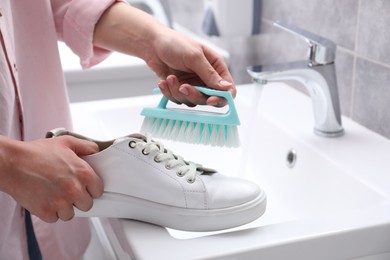 Photo of Woman washing stylish sneakers with brush in sink, closeup