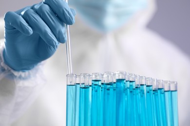 Scientist taking sample of light blue liquid on grey background, closeup