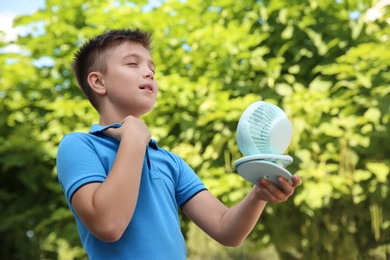 Photo of Little boy enjoying air flow from portable fan outdoors. Summer heat