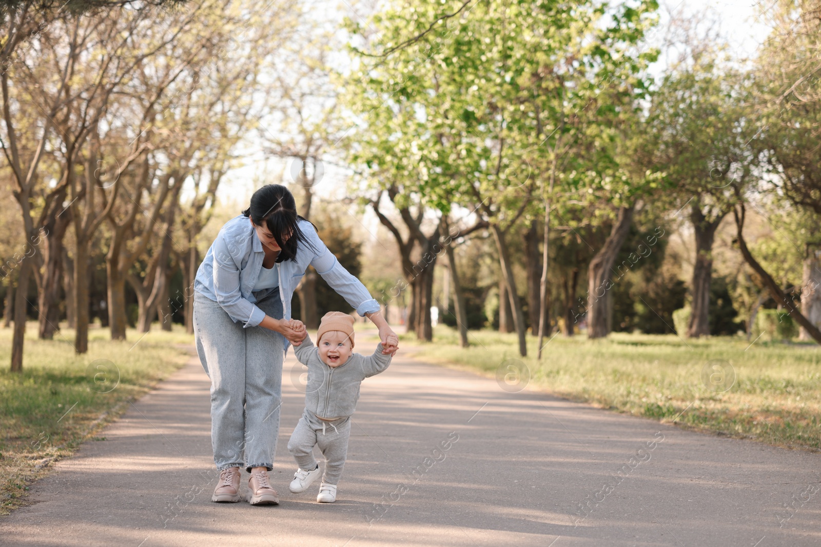 Photo of Mother supporting her baby while he learning to walk outdoors. Space for text