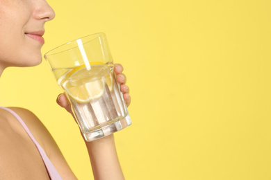 Photo of Young woman drinking lemon water on yellow background, closeup. Space for text