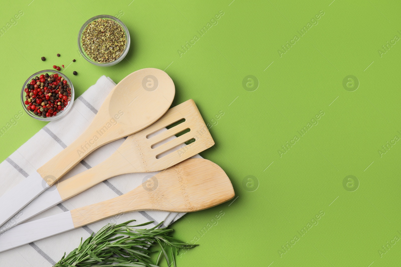 Photo of Set of wooden kitchen utensils and spices on green background, flat lay. Space for text