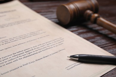 Photo of Last will and testament with pen near gavel on wooden table, closeup