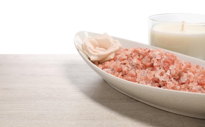 Natural sea salt in bowl, rose and candle on wooden table against white background. Space for text