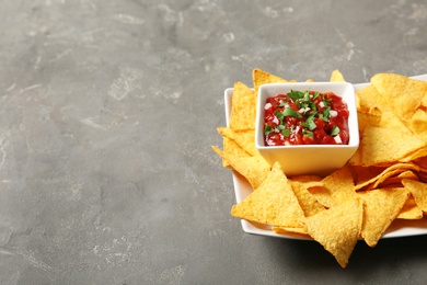 Photo of Plate with delicious mexican nachos chips and salsa sauce on grey table. Space for text