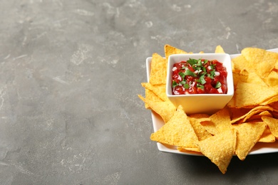 Plate with delicious mexican nachos chips and salsa sauce on grey table. Space for text