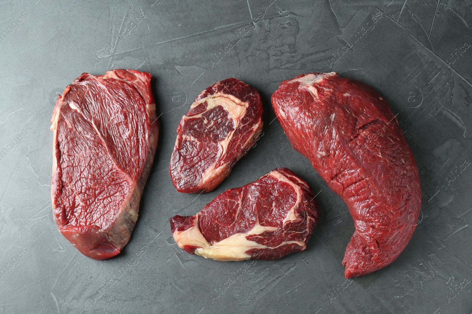 Photo of Pieces of raw beef meat on grey table, flat lay