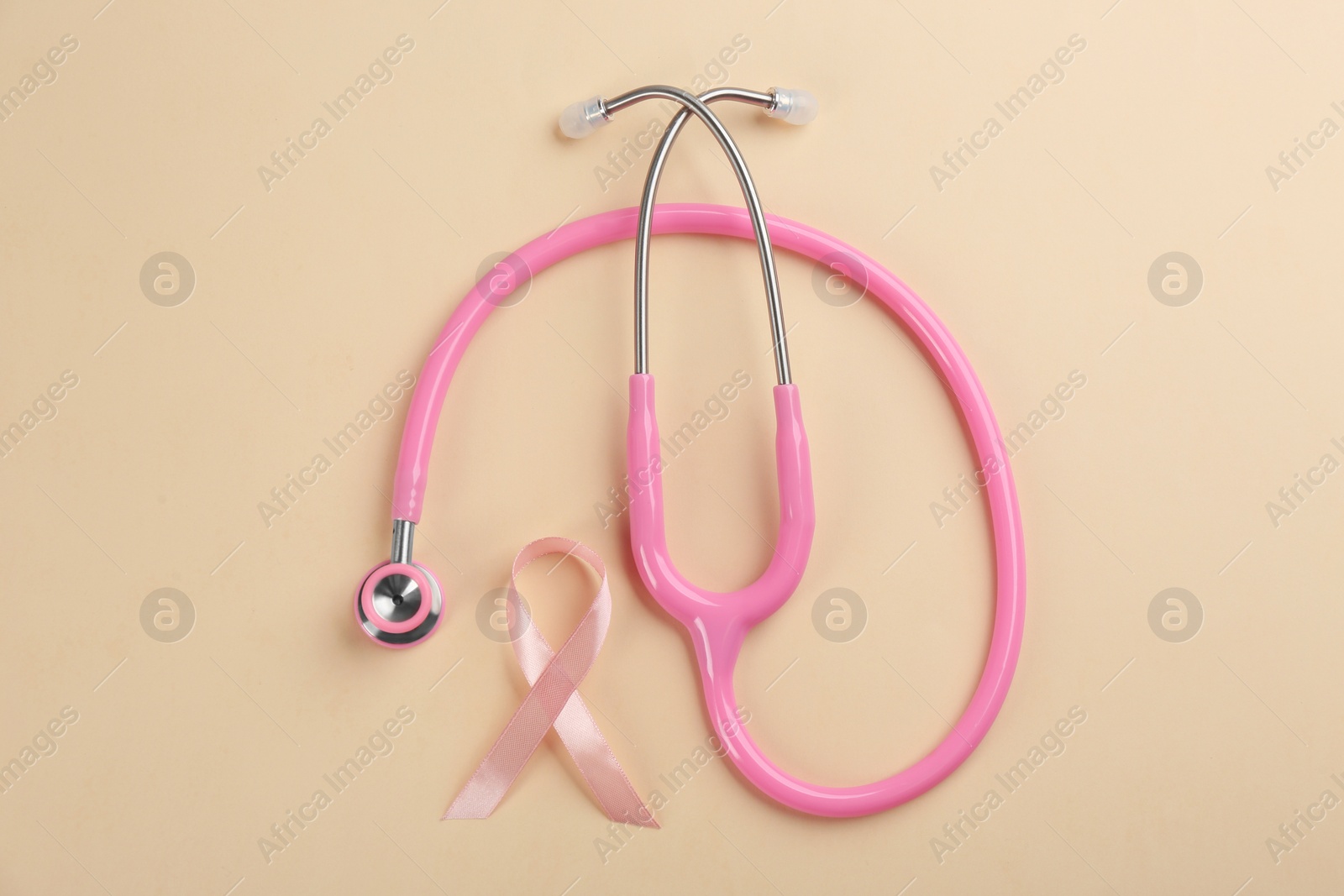 Photo of Pink ribbon and stethoscope on beige background, flat lay. Breast cancer concept