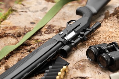 Hunting rifle, cartridges and binoculars on tree stump outdoors, closeup