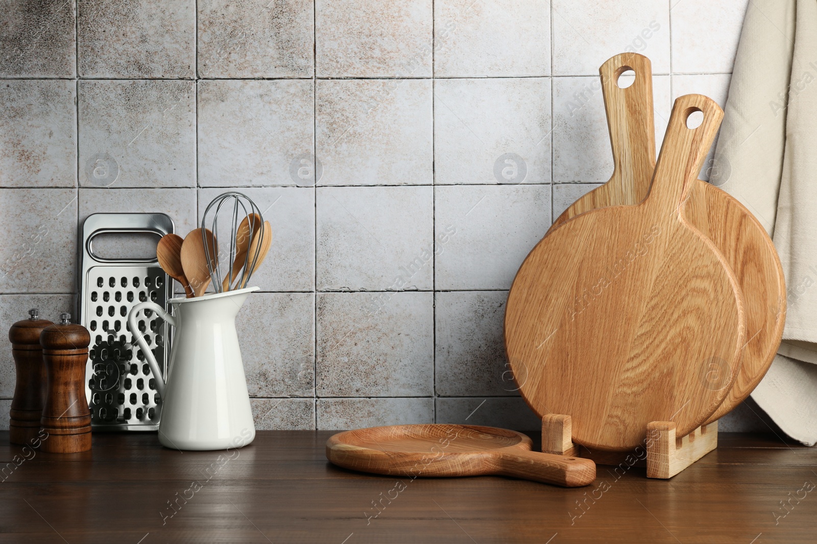Photo of Wooden cutting boards and kitchen utensils on table near tiled wall