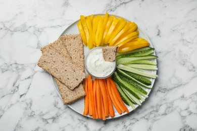 Photo of Plate with crispbreads, vegetable sticks and dip sauce on white marble table, top view