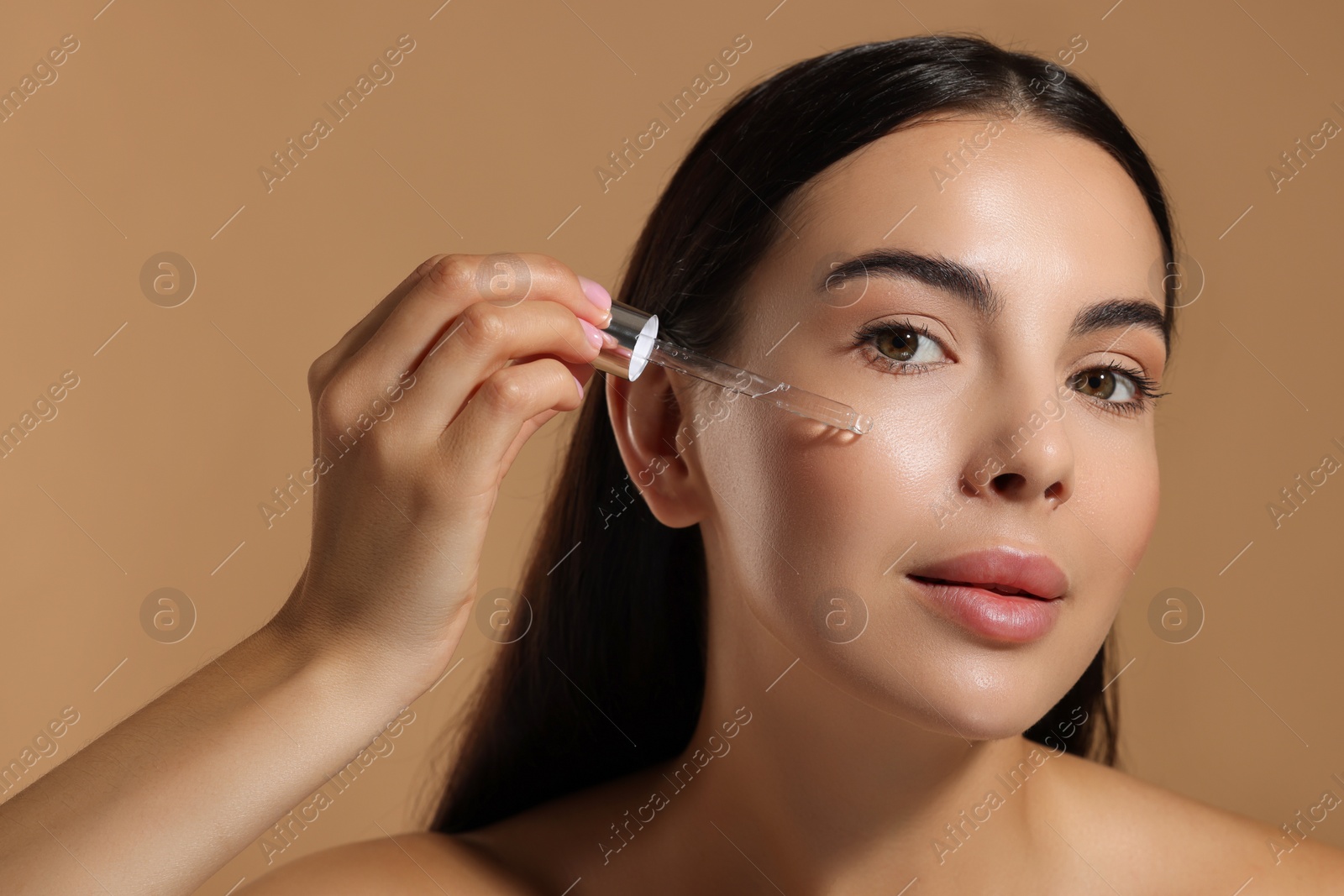 Photo of Beautiful young woman applying serum onto her face on beige background