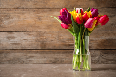 Photo of Beautiful spring tulips in vase on table against wooden background. Space for text