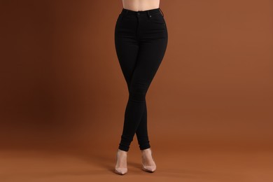 Photo of Woman wearing stylish black jeans and high heels shoes on brown background, closeup