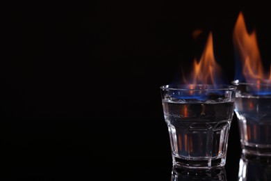 Photo of Flaming vodka in shot glasses on black background, space for text